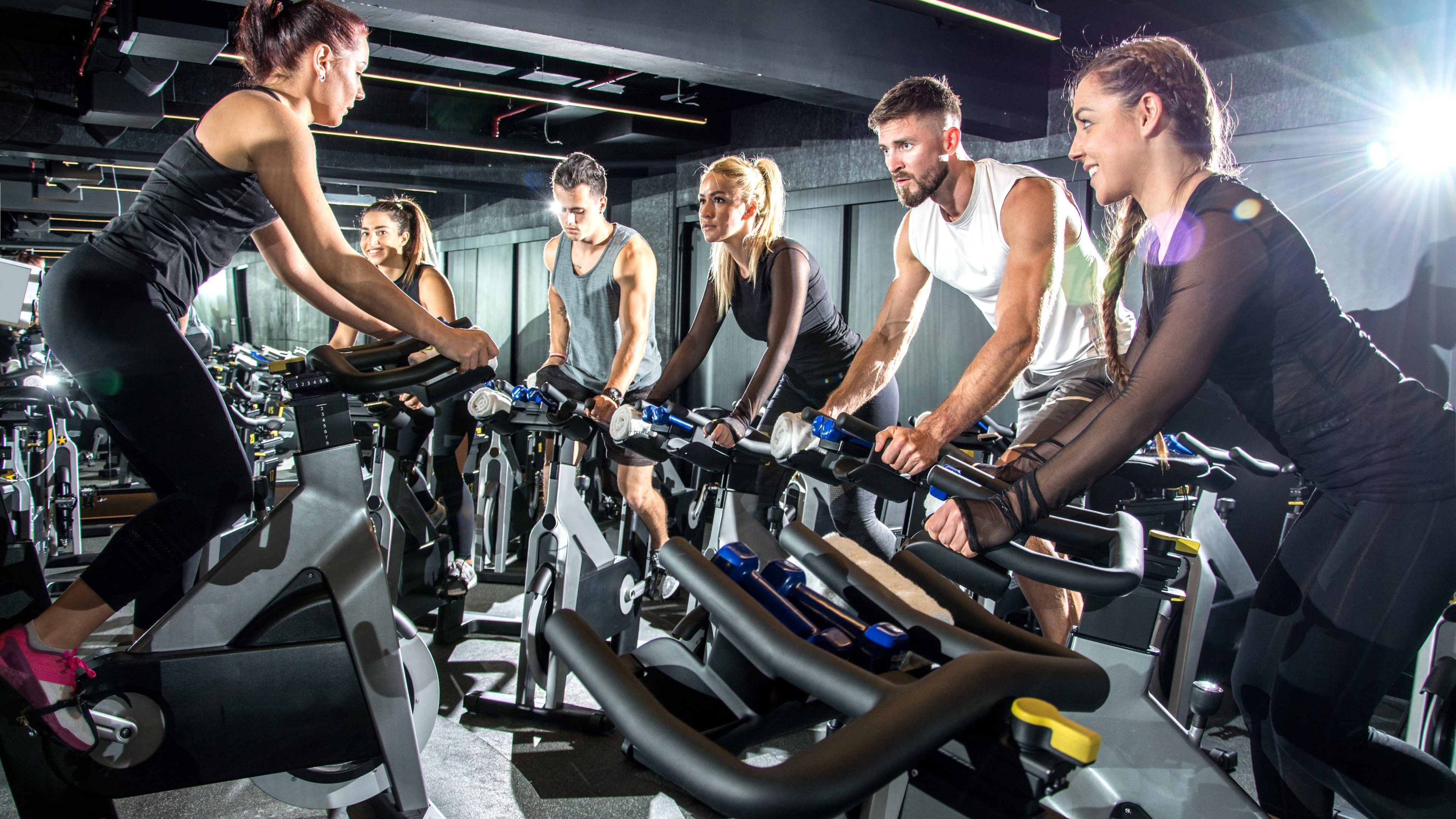 Group of sporty women and men training on exercise bikes together at gym.