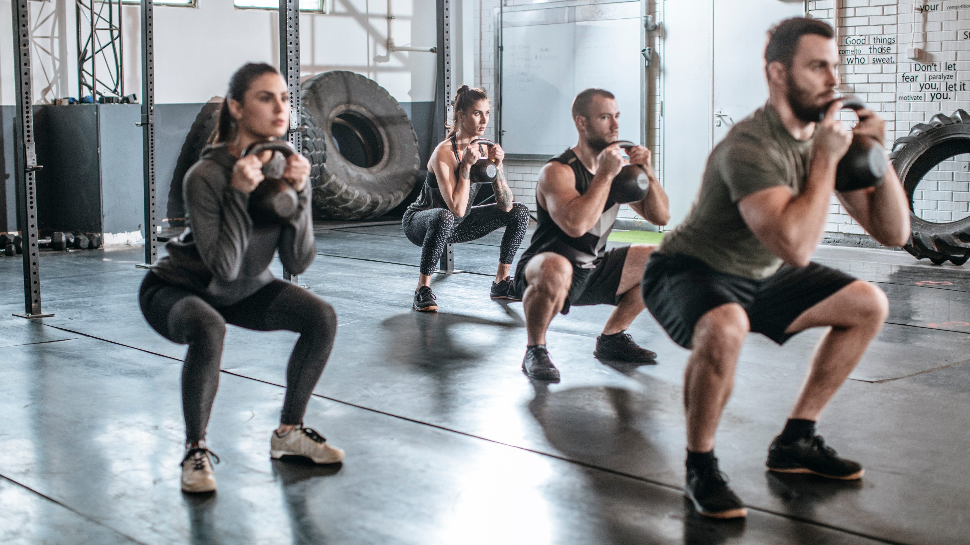 Group of people lifting weights at crossfit training at gym.